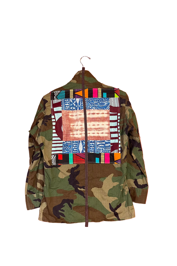 Camouflage jacket with colorful patchwork design on a hanger against an orange wall