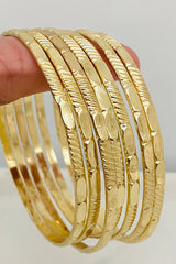 Gold bangles stacked on a finger against a neutral background