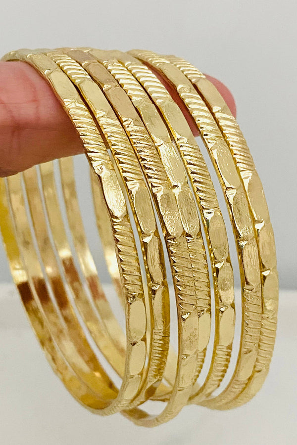 Gold bangles stacked on a finger against a neutral background
